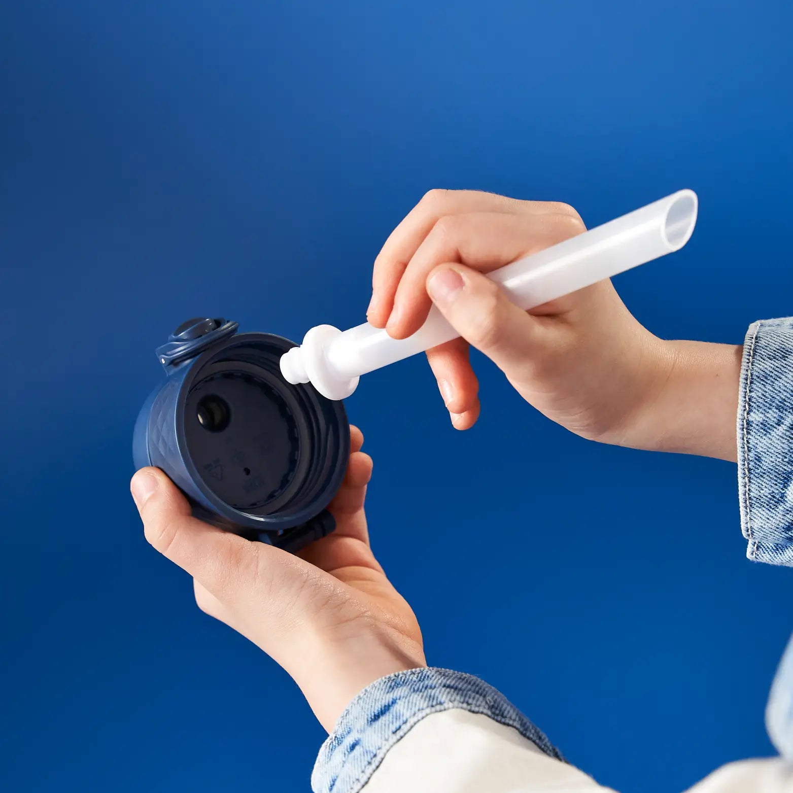 A person cleans a blue water bottle lid with a white cleaning tool against a blue background.