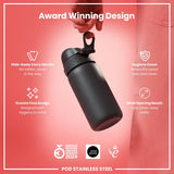 A dark gray, cylindrical water bottle is being held. Its features include a hidden handle, a hygiene cover, and a wide mouth. The background is a coral pink. The bottle is described as an award-winning design.
