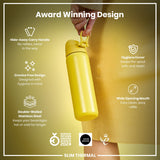 A yellow, double-walled stainless steel water bottle is held by a person wearing a mustard yellow top. The bottle features a hide-away handle, crevice-free design, hygiene cover, and wide opening mouth. It's an award-winning design.