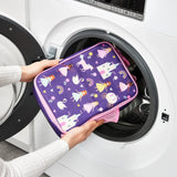 Hands placing a colorful princess-themed bag featuring castles, unicorns, and rainbows into a front-loading washing machine in a laundry setting.