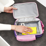 Hand cleans pink lunchbox interior with yellow sponge on dark countertop near white sink
