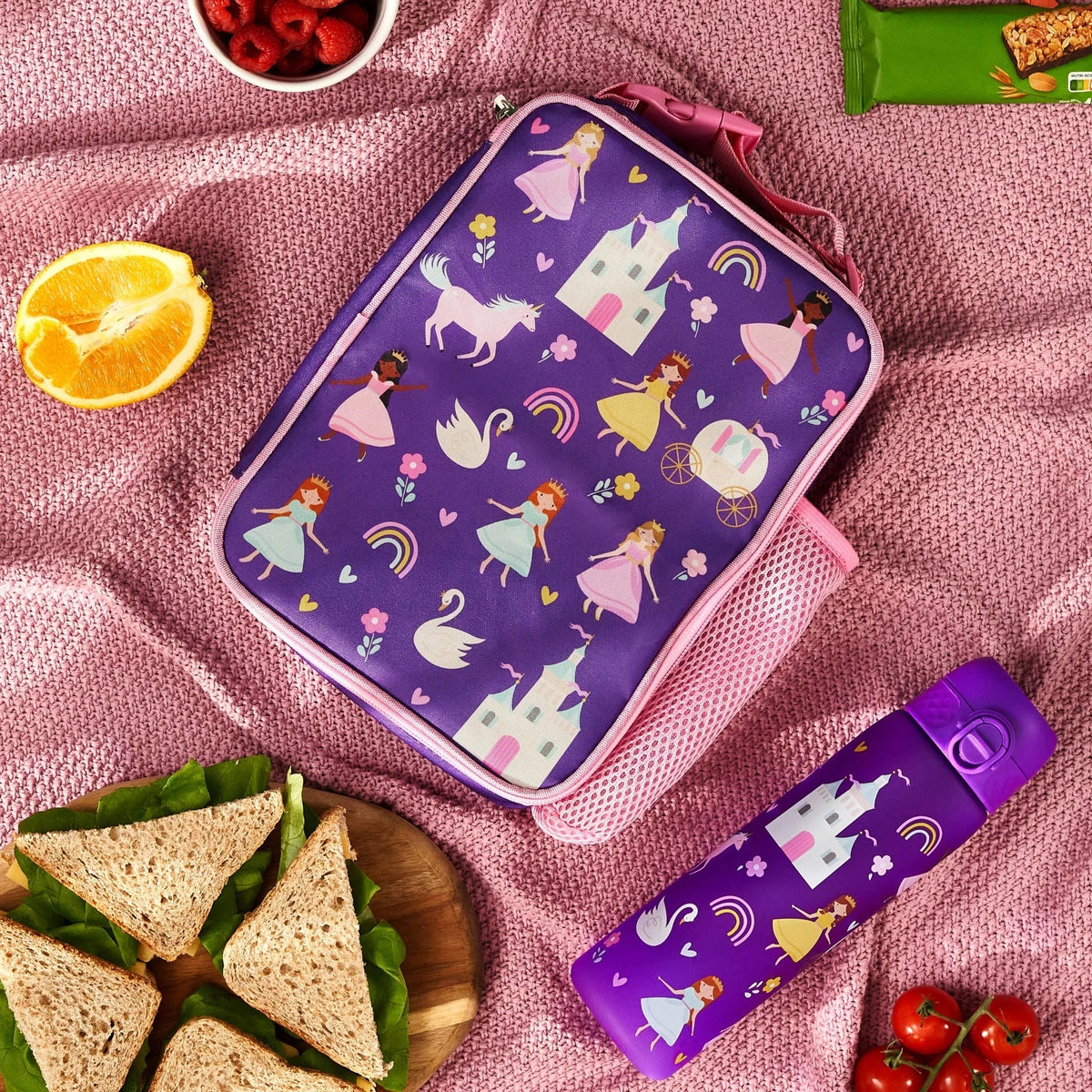 Lunchbox adorned with princess-themed illustrations resting on a pink blanket surrounded by a purple water bottle, sandwich, orange slice, and bowl of raspberries.