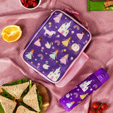 Lunchbox adorned with princess-themed illustrations resting on a pink blanket surrounded by a purple water bottle, sandwich, orange slice, and bowl of raspberries.