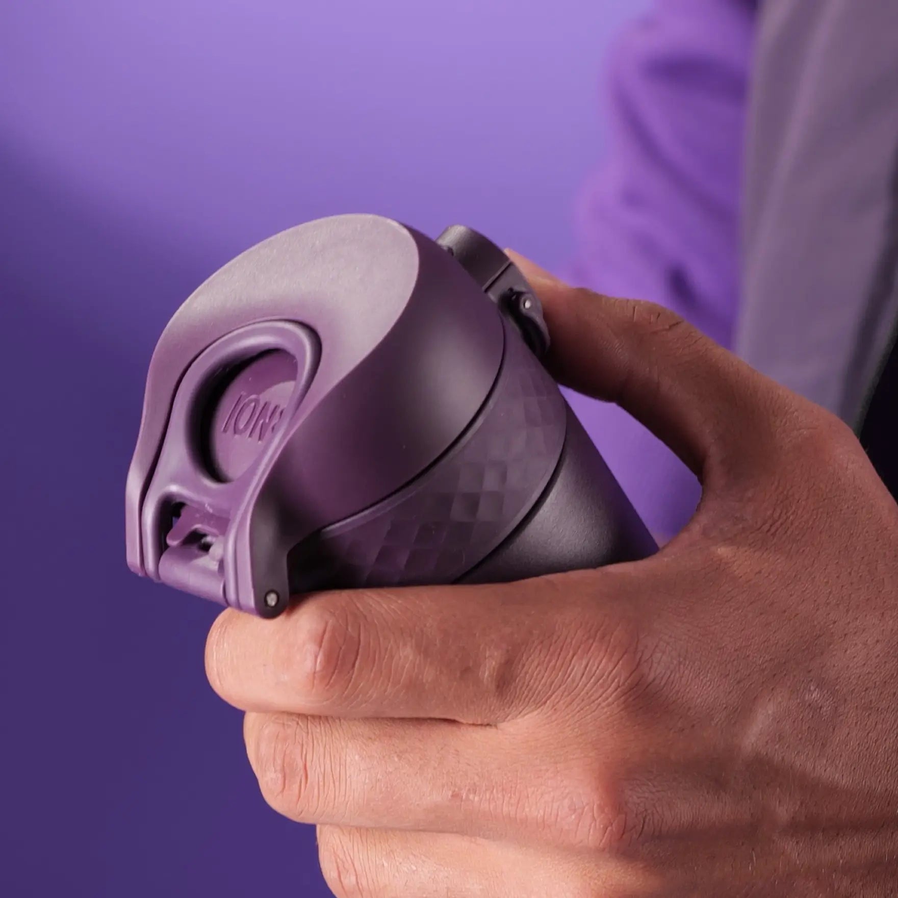 A purple ION8 travel mug is held in a person's hand against a purple background.