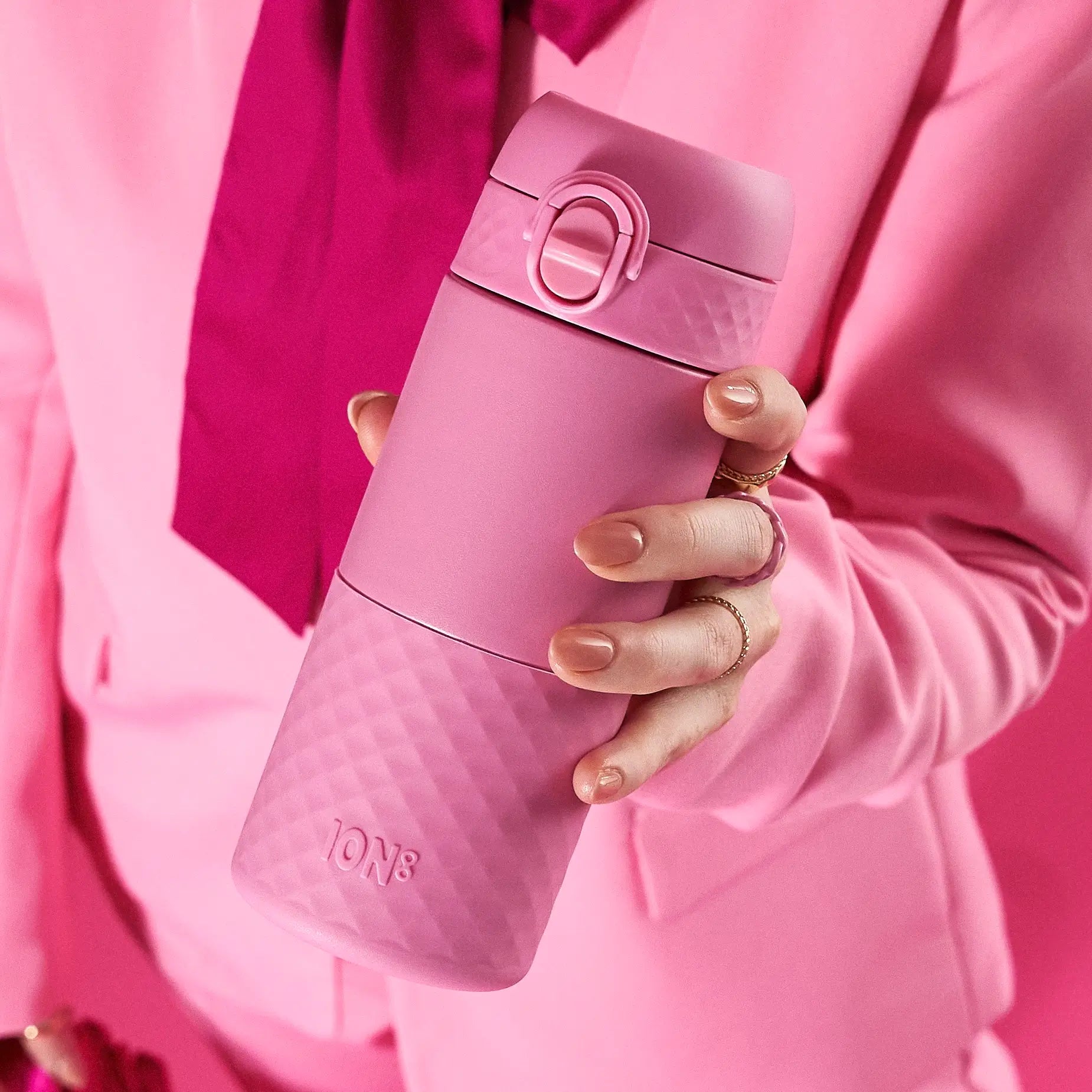 A pink, textured ION8 water bottle is held in a hand. The hand and the bottle are both visible against a pink garment.