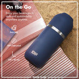 A blue ION8 travel flask lies on a striped cloth beside sunglasses on sand Text: 