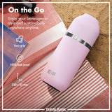 A pink travel flask with a black band rests on a red-striped towel by the sand. Text: 