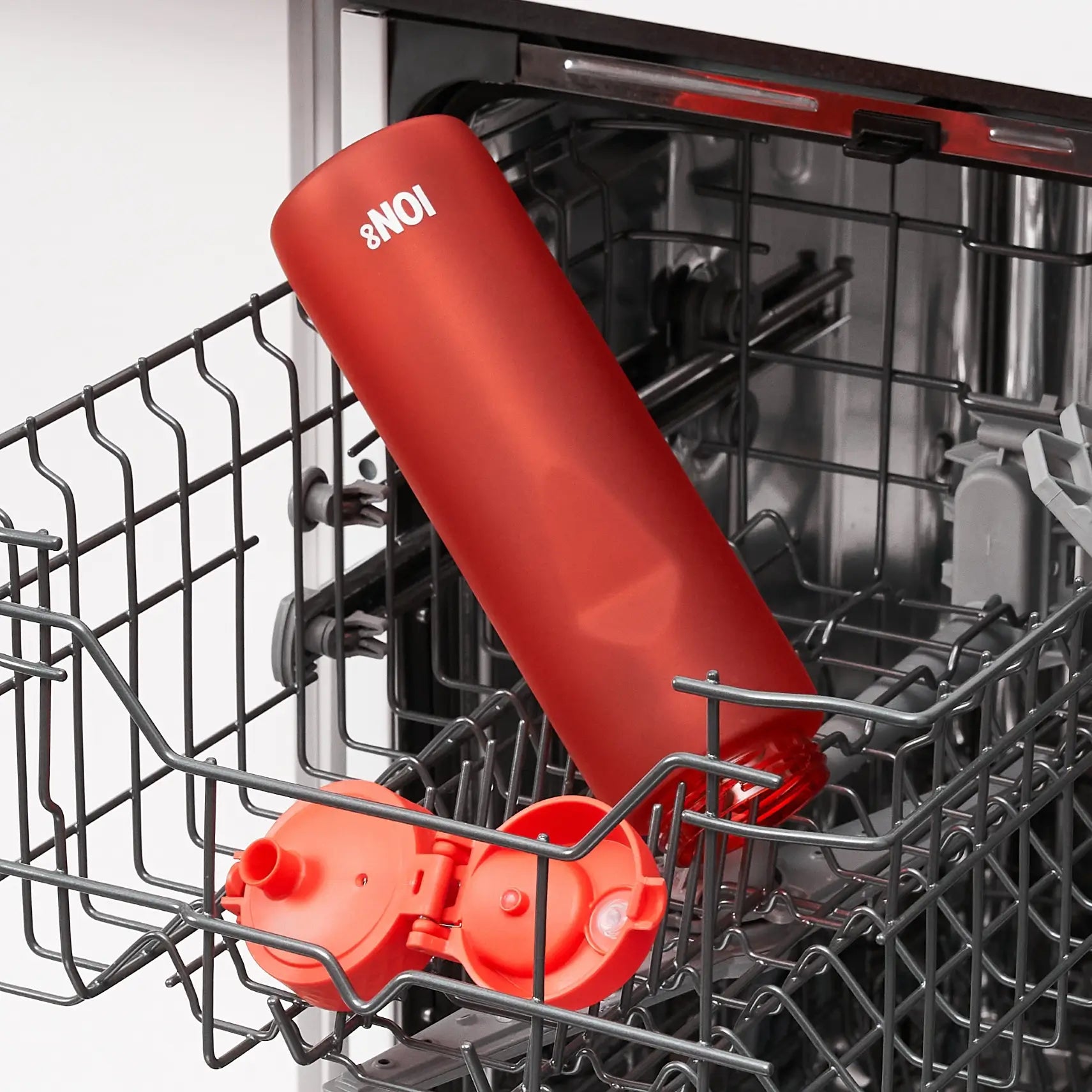 A red ION8 water bottle is being washed inside a dishwasher's wire rack.