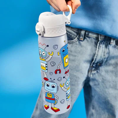 A water bottle, featuring cartoon robots, is being held against a bright blue background. The person holding it wears light blue jeans.