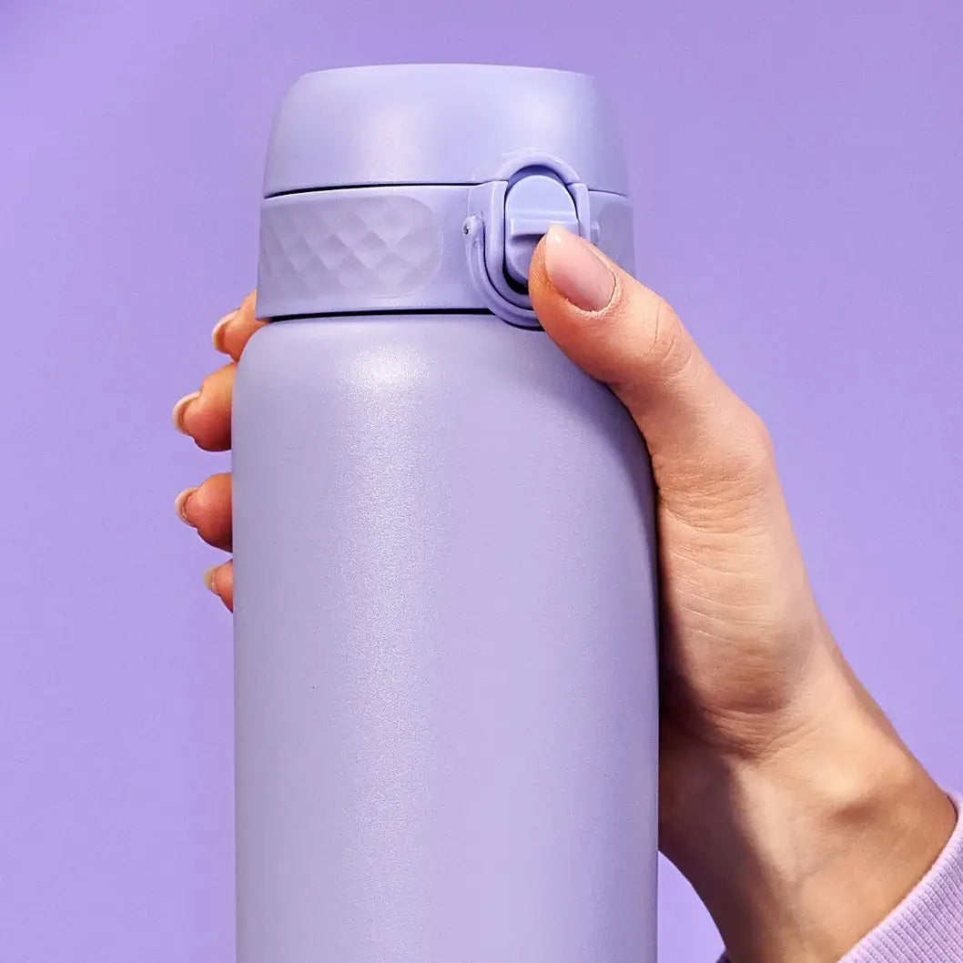 A lavender-colored water bottle is held; a person's hand presses the lid. The background is a solid, matching lavender color.