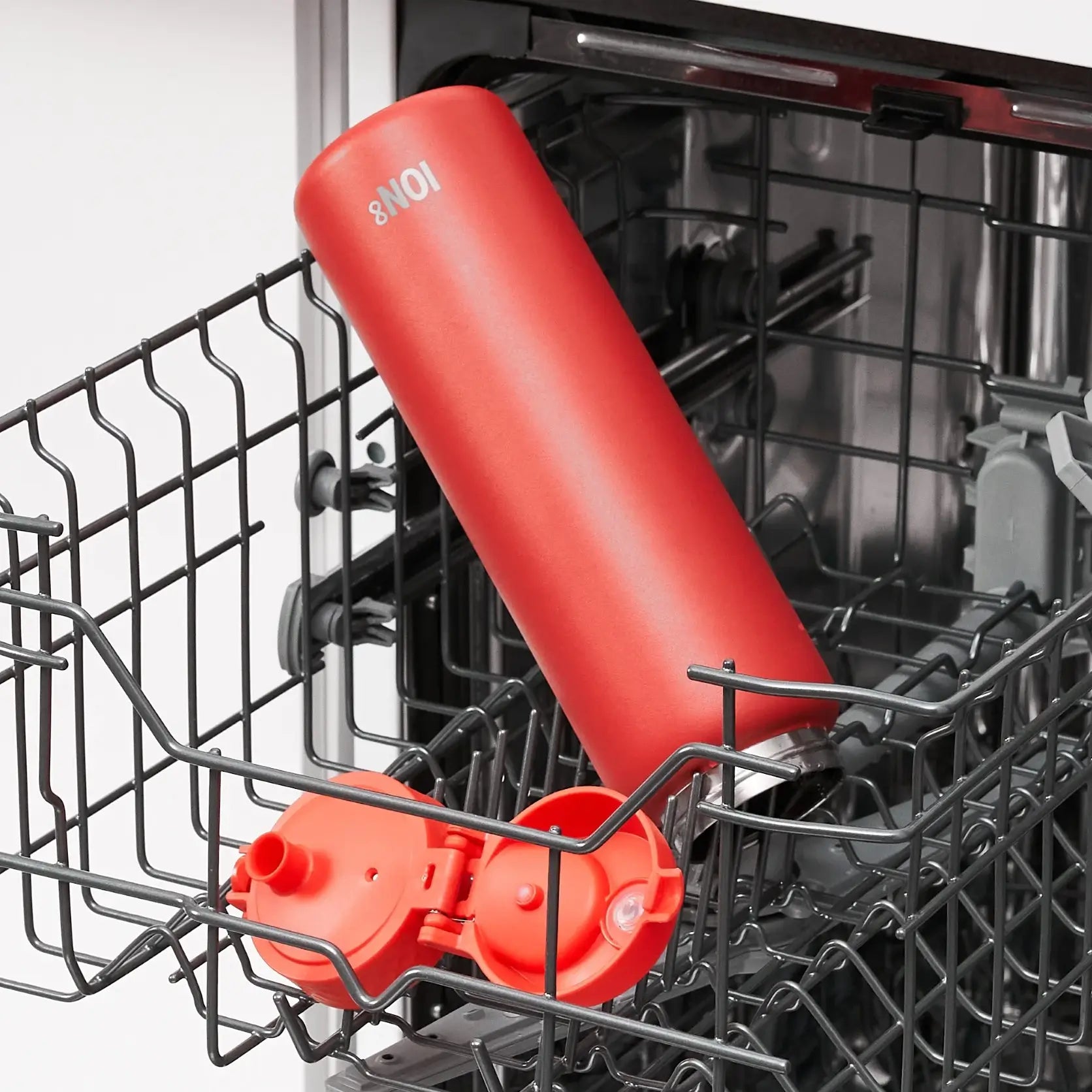 A red ION8 water bottle is being cleaned inside a dishwasher's upper rack. Two red lids are also present.