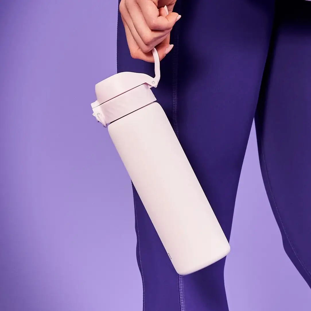 A person holds a light pink water bottle with a hinged lid against a purple background.