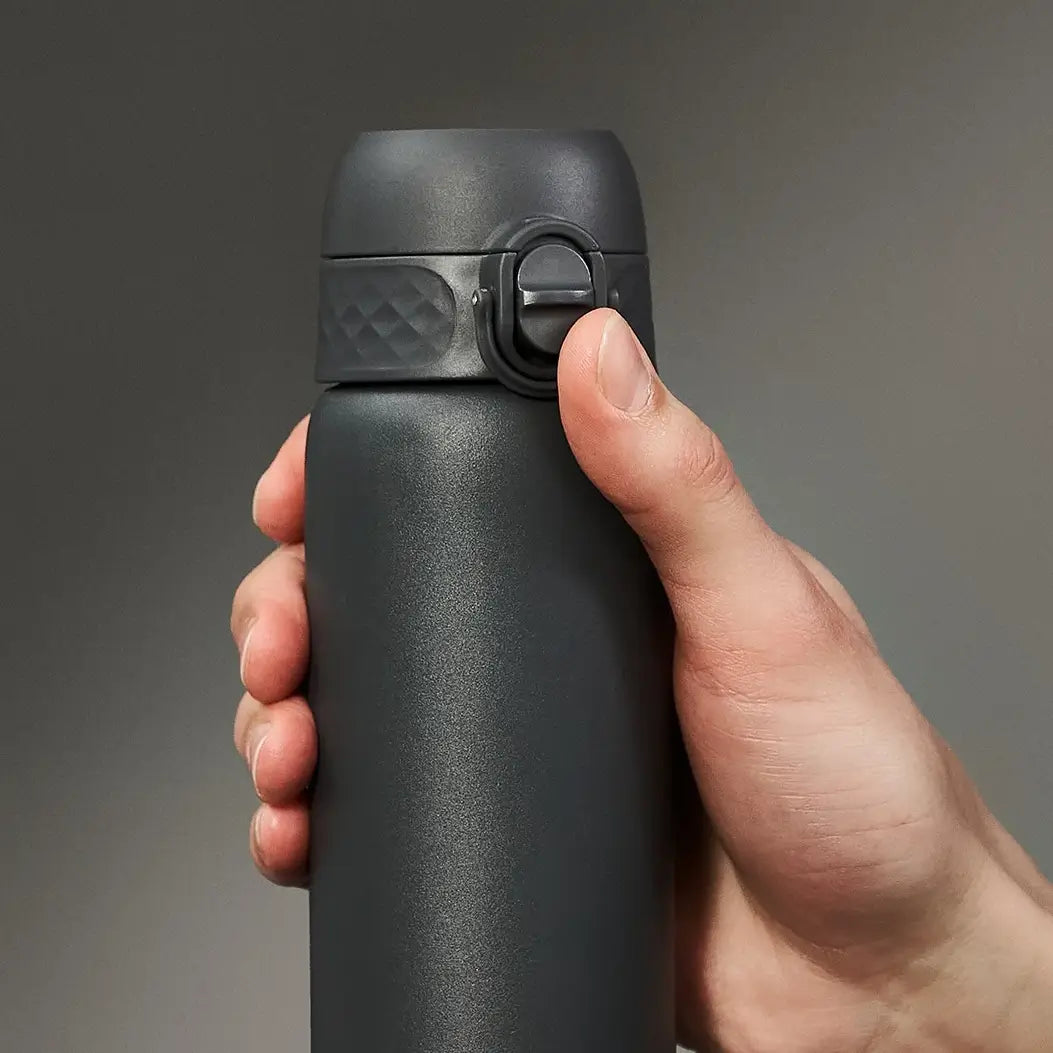 A dark grey thermos is being held and opened by a hand against a muted background.