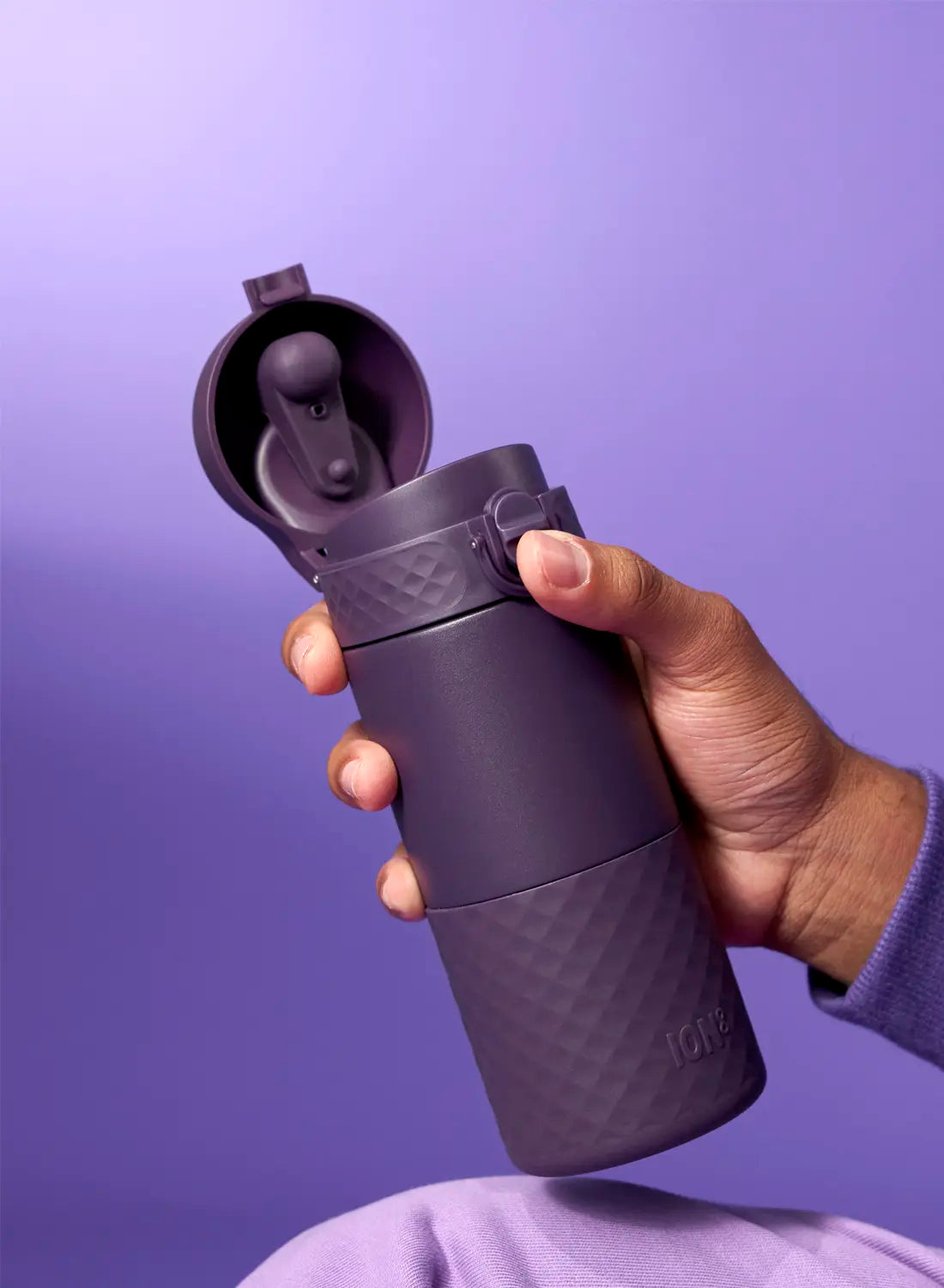 A purple, textured ION8 thermos is being held; its lid is open, revealing an internal mechanism. The hand and thermos are against a purple background.